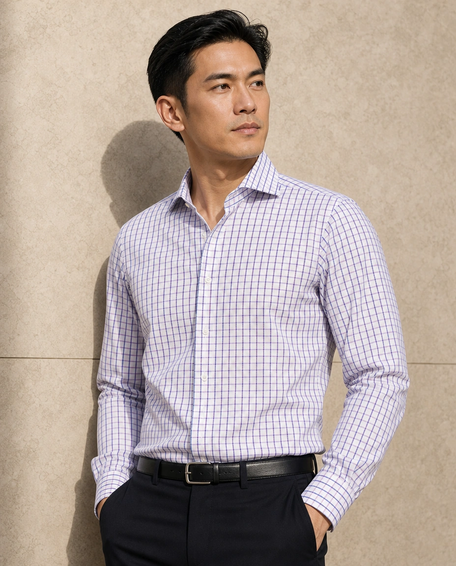 A model against a sunlit stone wall in a blue checked long-sleeved shirt and black trousers