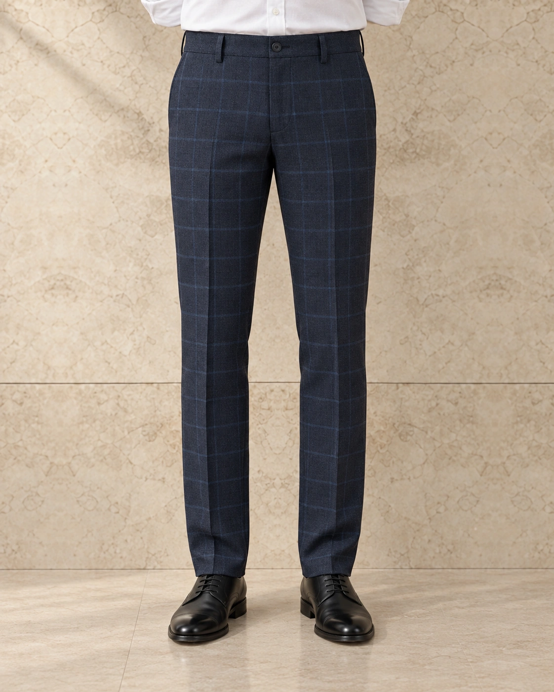 A model from the waist down against a sunlit stone wall, in navy check trousers on a single-button waistband, flat-fronted, mid rise and slim tapered over black lace-ups