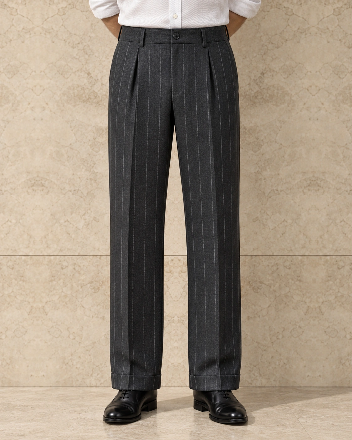 A model from the waist down against a sunlit stone wall, in charcoal chalk stripe trousers on a single-button waistband, single-pleated, high rise and wide-legged with turn-ups over black lace-ups