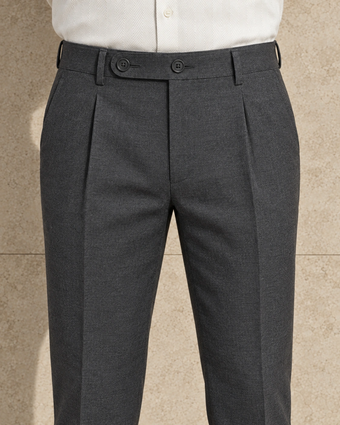 A close view from waist to knee of mid grey trousers, single-pleated and fastened on an extended tab with two buttons