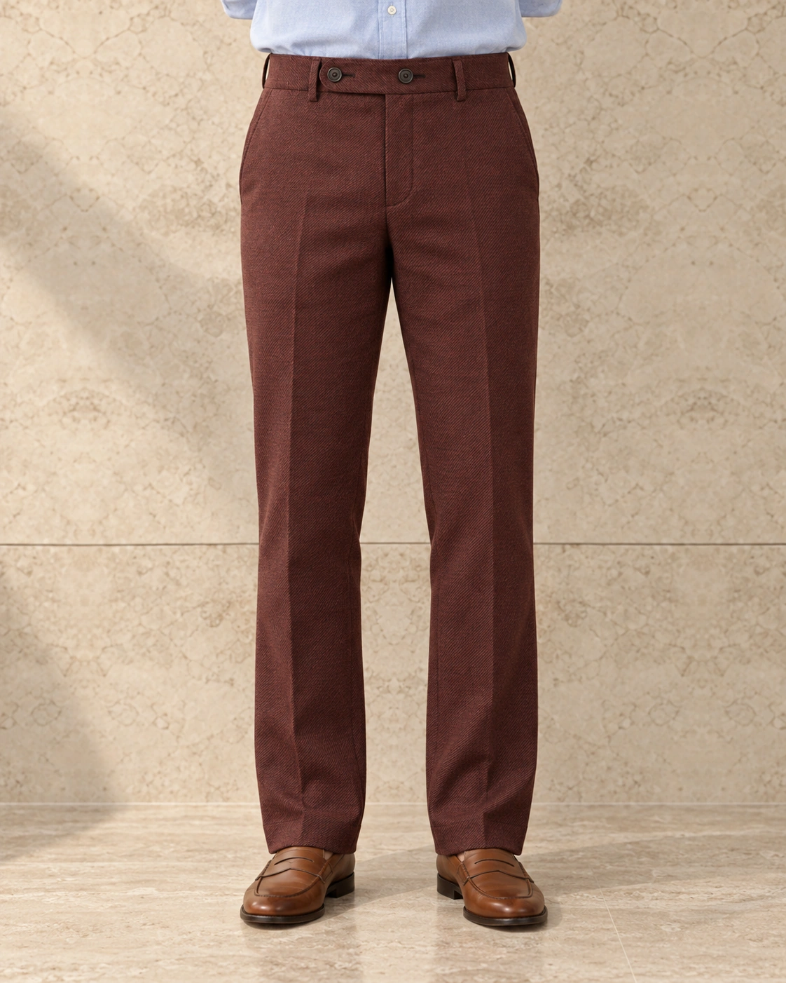 A model from the waist down against a sunlit stone wall, in rust trousers on an extended tab with two buttons, flat-fronted, high rise and straight-legged over tan loafers