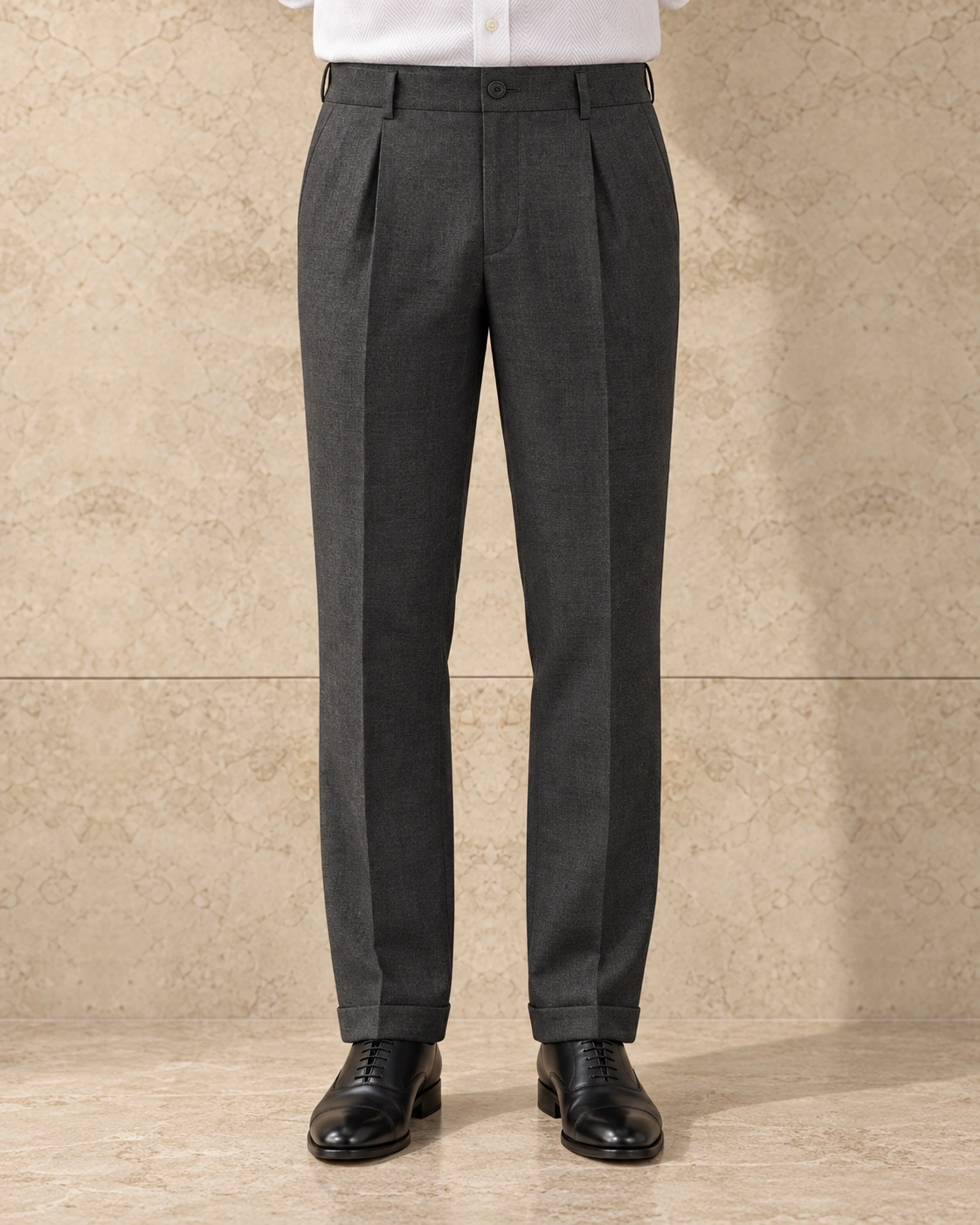 A model from the waist down against a sunlit stone wall, in charcoal trousers on a single-button waistband, single-pleated, mid rise and tapered with turn-ups over black lace-ups