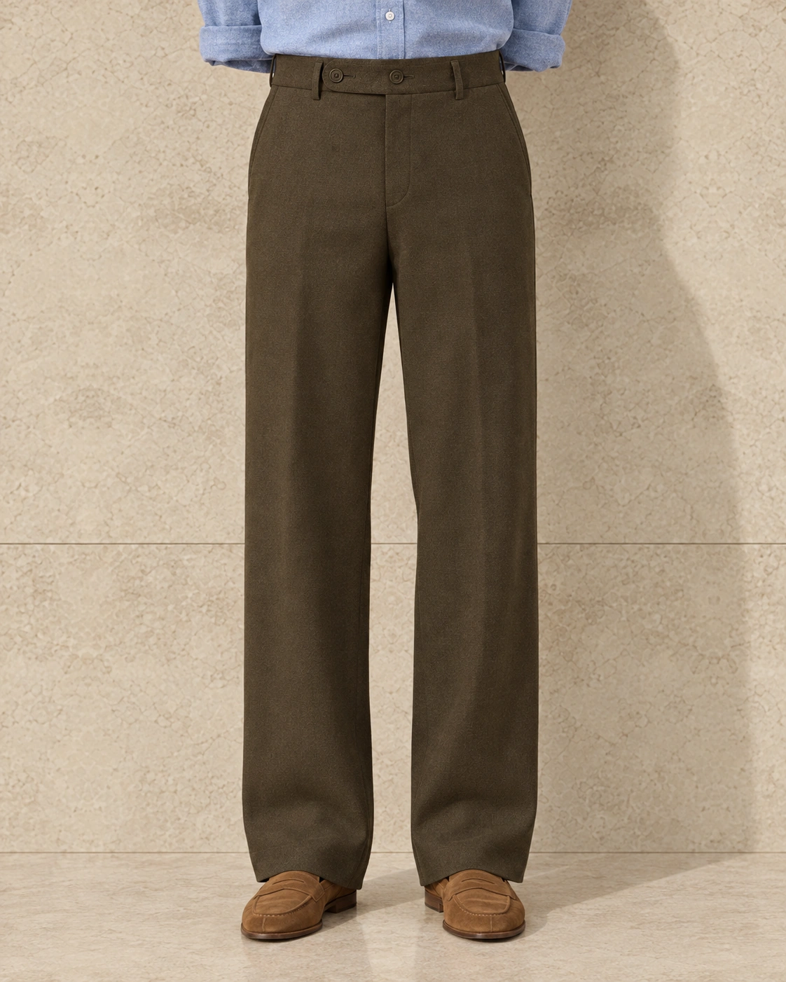 A model from the waist down against a sunlit stone wall, in khaki trousers on an extended tab with two buttons, flat-fronted, high rise and wide-legged over tan suede loafers