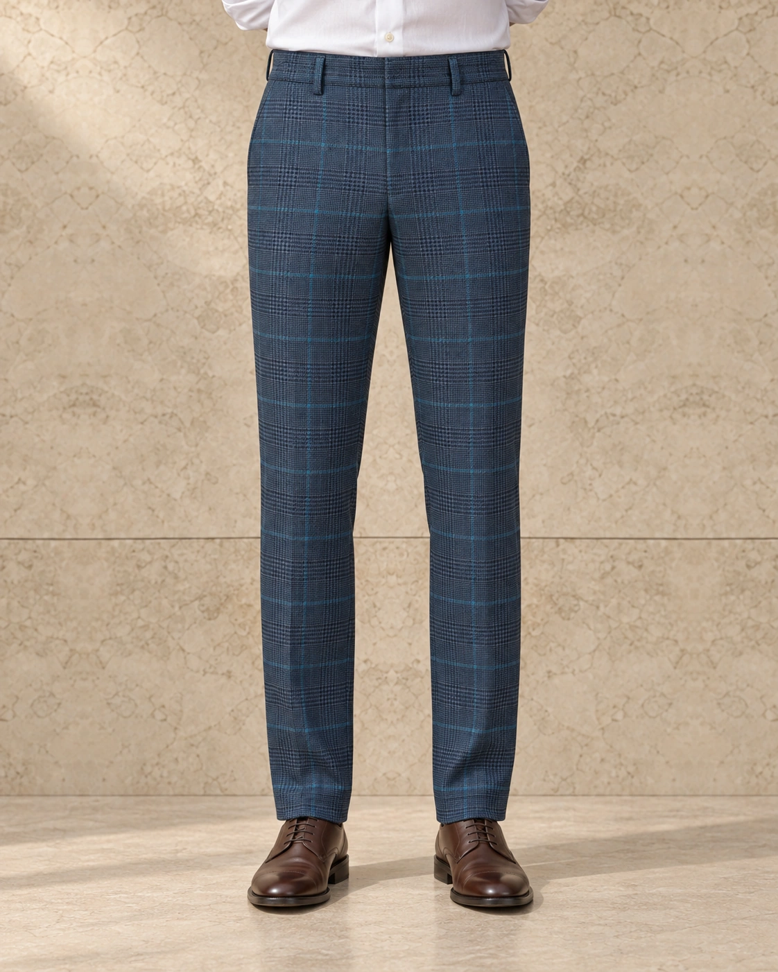 A model from the waist down against a sunlit stone wall, in teal check trousers on a plain waistband closed with a hook and bar, flat-fronted, mid rise and tapered over brown lace-ups