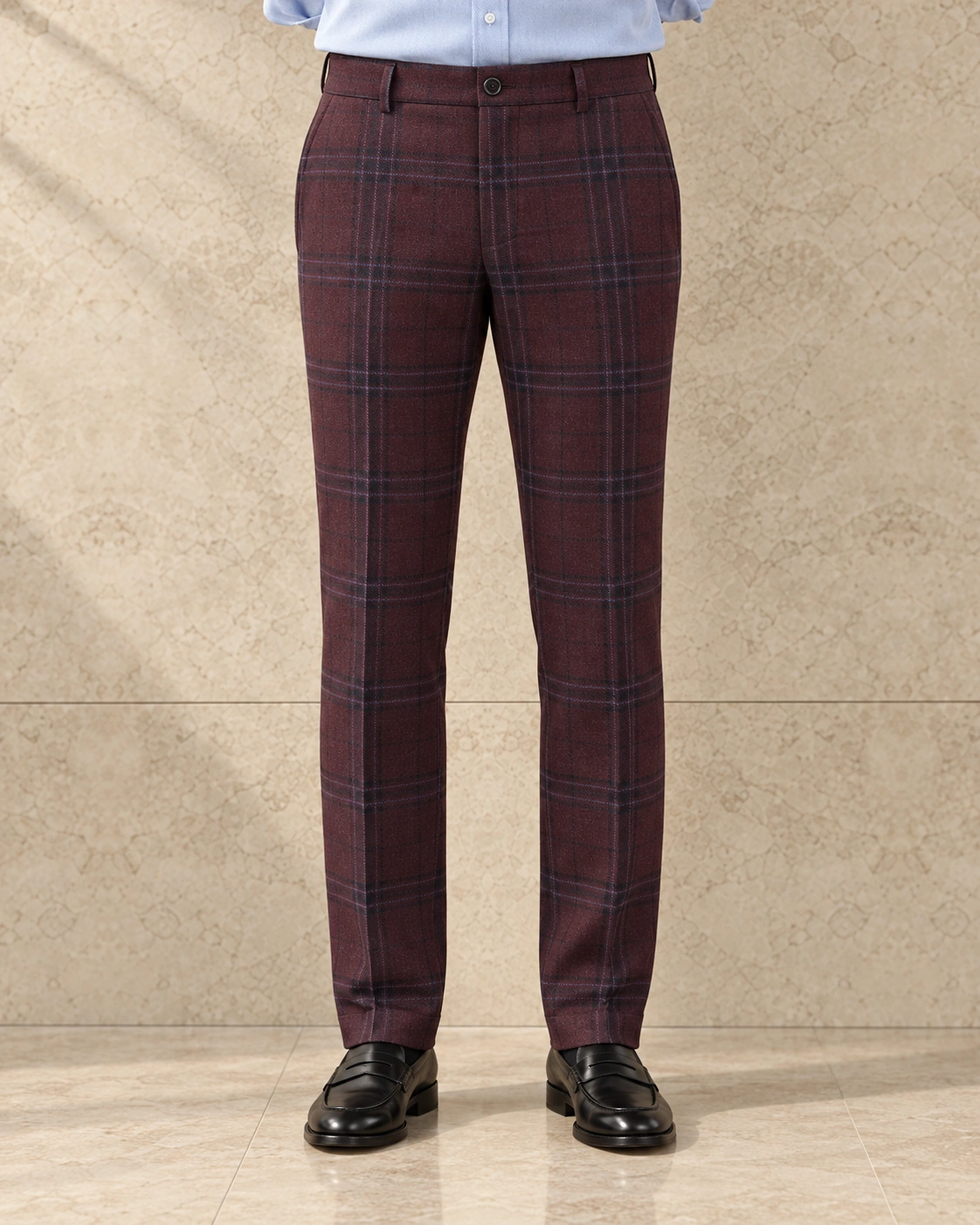 A model from the waist down against a sunlit stone wall, in burgundy check trousers on a single-button waistband, flat-fronted, low rise and tapered over black loafers